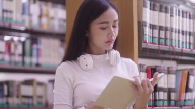 Üniversite kütüphanesinde kitaplığın yanında oturan Asyalı kadın ya da öğrenci kitapları, eğitim konsepti