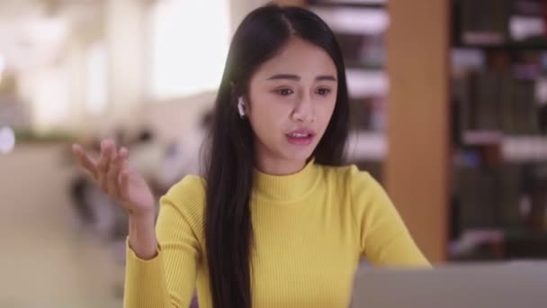 アジアの女性学生は オンラインでヘッドフォンのトークビデオコールをラップトップコンピュータスクリーンで着用し チューターとの会議 または図書館でのウェビナーエラークラスのEラーニングコースを行います 高品質の4K映像 — ストック動画