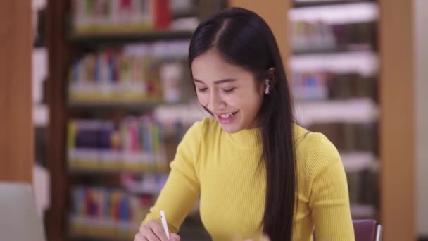 一位迷人的年轻亚洲少女在图书馆学习在线课程 她用平板电脑和笔记本电脑搜索网上考试信息 高质量的4K镜头 — 图库视频影像