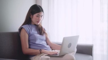 Sosyal medyada sörf yapan güzel bir Asyalı kadın ya da evdeki oturma odasında dinlenirken dizüstü bilgisayarda çalışan bir kadın oturma odasında faaliyet kavramı. Yüksek kalite 4k görüntü
