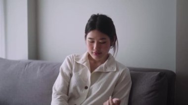 Genç Asyalı kadın elinde bir bardak suyla ilaç alıyor. Kanepede otururken Akut Ağrı hissediyor. Sağlık sigortası ve insanların konsepti. Yüksek kalite 4k görüntü