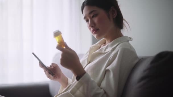 Zieke Aziatische Vrouw Met Een Pil Fles Lezen Informatie Geneesmiddel — Stockvideo