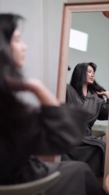 An Asian woman blow-drying her hair in front of a large mirror after washing and styling it at home. Capture the essence of beauty and self-care. High quality 4k footage