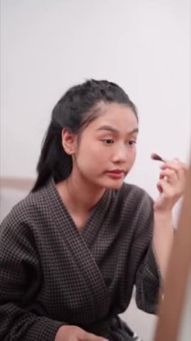 Asian woman applying eyeshadow in front of a large mirror after bathing and styling her hair at home. Showcase her beauty routine. High quality 4k footage
