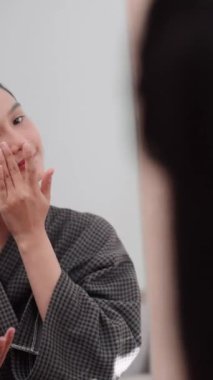 Asian woman applying face powder in front of a large mirror after washing and styling her hair at home. Showcase her beauty routine for enhanced sales and skincare awareness