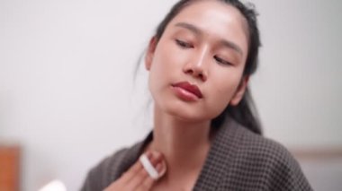 Asian woman applying face powder in front of a large mirror after washing and styling her hair at home. Showcase her beauty routine for enhanced sales and skincare awareness. High quality 4k footage