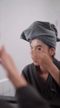 Asian woman is applying facial foam in front of a bathroom mirror, getting ready for a refreshing shower. Capture daily skincare routines and self-care moments for a radiant image