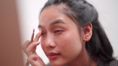 Asian woman applying eyeshadow in front of a large mirror after bathing and styling her hair at home. Showcase her beauty routine. High quality 4k footage