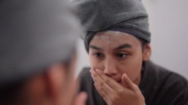 Asian woman is applying facial foam in front of a bathroom mirror, getting ready for a refreshing shower. Capture daily skincare routines and self-care moments for a radiant image
