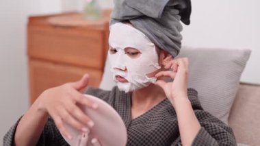 An Asian woman is applying a face mask for a rejuvenating skincare routine, nurturing her skins health and radiance at her home. Capture the essence of self-care and wellness