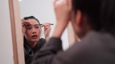 Asian woman applying eyeliner in front of a large mirror after bathing and styling her hair at home. Capture her beauty routine. High quality 4k footage