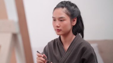 Asian woman applying eyeliner in front of a large mirror after bathing and styling her hair at home. Capture her beauty routine. High quality 4k footage