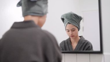 Asian woman is applying facial foam in front of a bathroom mirror, getting ready for a refreshing shower. Capture daily skincare routines and self-care moments for a radiant.