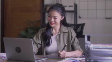 Young Asian Women Graphic designer Artist work on computer laptop and with graphic interactive drawing pen sitting in front of window at desk in office. High quality 4k footage