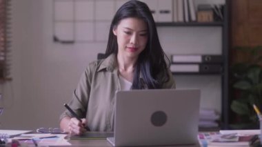 Young Asian Women Graphic designer Artist work on computer laptop and with graphic interactive drawing pen sitting in front of window at desk in office. High quality 4k footage