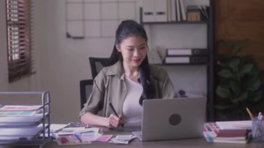Young Asian Women Graphic designer Artist work on computer laptop and with graphic interactive drawing pen sitting in front of window at desk in office. High quality 4k footage
