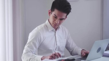 Serious Asian businessman in office using calculator and laptop for work and calculate financial expenses at workplace. High quality 4k footage
