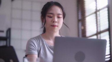 Young Asian woman hard working with documents at her using laptop computer with analytical charts and graphs at her home, work from home concept. High quality 4k footage