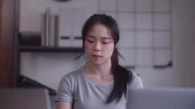 Young Asian woman hard working with documents at her using laptop computer with analytical charts and graphs at her home, work from home concept. High quality 4k footage