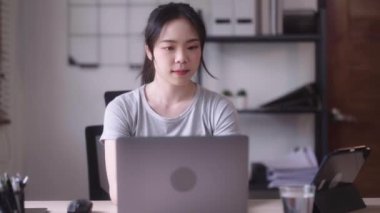 Young Asian woman hard working with documents at her using laptop computer with analytical charts and graphs at her home, work from home concept. High quality 4k footage