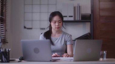 Young Asian woman hard working with documents at her using laptop computer with analytical charts and graphs at her home, work from home concept. High quality 4k footage
