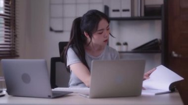 Young Asian woman hard working with documents at her using laptop computer with analytical charts and graphs at her home, work from home concept. High quality 4k footage