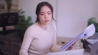 Young Asian woman hard working with documents at her using laptop computer with analytical charts and graphs at her home, work from home concept. High quality 4k footage