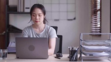 Masasında dizüstü bilgisayarla çalışırken Asyalı bir kadın oturma odasında oturuyor..