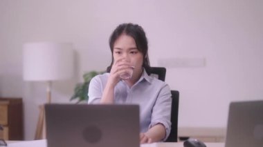 Evdeki ofiste bir bardak su içerken dizüstü bilgisayarla çalışan çekici Asyalı bir iş kadını. Yüksek kalite 4k görüntü