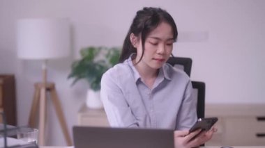 Genç Asyalı iş kadını cep telefonuyla konuşuyor ya da ev ofisinde çalışırken kurumsal iş sorununu çözmek için akıllı telefon kullanıyor. Yüksek kalite 4k görüntü