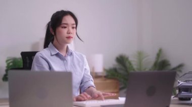 Masasında dizüstü bilgisayarla çalışırken oturma odasında oturan rahat, genç Asyalı kadın..
