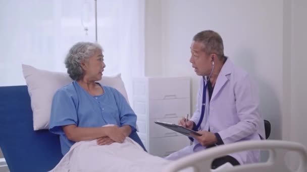 Senior Asiatisk Man Läkare Sitter Vid Skrivbordet Och Håller Stetoskop — Stockvideo
