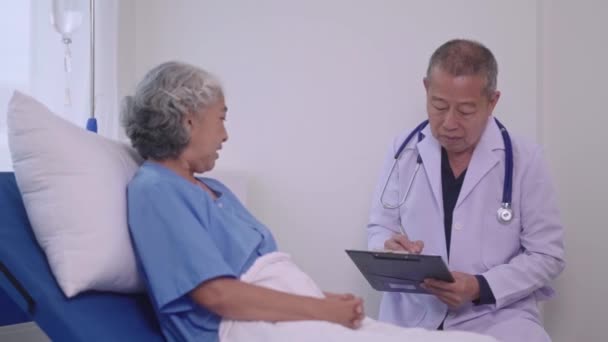 资深亚洲男子医生在诊疗所与检查室的老年妇女病人进行的医疗检查 医疗保健或医院支助过程中交谈 高质量的4K镜头 — 图库视频影像