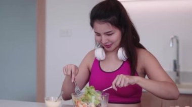 Spor giyimli genç Asyalı sporcu kadın sağlıklı bir salata yapıyor evdeki mutfakta yeşil sebzeleri karıştırarak sağlıklı bir diyet konseptini inceliyor. Yüksek kalite 4k görüntü