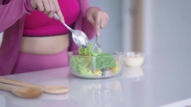 Spor giyimli genç Asyalı sporcu kadın sağlıklı bir salata yapıyor evdeki mutfakta yeşil sebzeleri karıştırarak sağlıklı bir diyet konseptini inceliyor. Yüksek kalite 4k görüntü