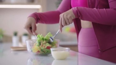 Spor giyimli genç Asyalı sporcu kadın sağlıklı bir salata yapıyor evdeki mutfakta yeşil sebzeleri karıştırarak sağlıklı bir diyet konseptini inceliyor. Yüksek kalite 4k görüntü