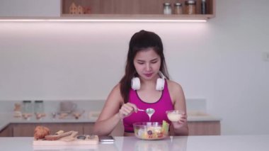 Spor giyimli genç Asyalı sporcu kadın sağlıklı bir salata yapıyor evdeki mutfakta yeşil sebzeleri karıştırarak sağlıklı bir diyet konseptini inceliyor. Yüksek kalite 4k görüntü