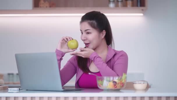 スポーツウェアのスポーツウェアのスポーツ若いアジアの女性は健康的な食事をしながらラップトップを介してオンラインビデオ通話を持っています — ストック動画