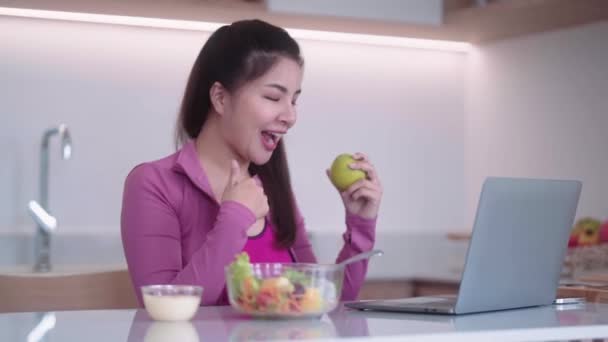 スポーツウェアのスポーツウェアのスポーツ若いアジアの女性は健康的な食事をしながらラップトップを介してオンラインビデオ通話を持っています — ストック動画