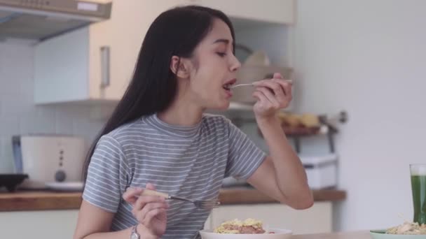 ハッピーミール アジアの女性がフォークとスプーンを持ってプレートとテーブルにアジアの食べ物米を食べる本物のエキゾチックな自家製の健康的なタイ料理を自宅で楽しんでください 高品質の4K映像 — ストック動画