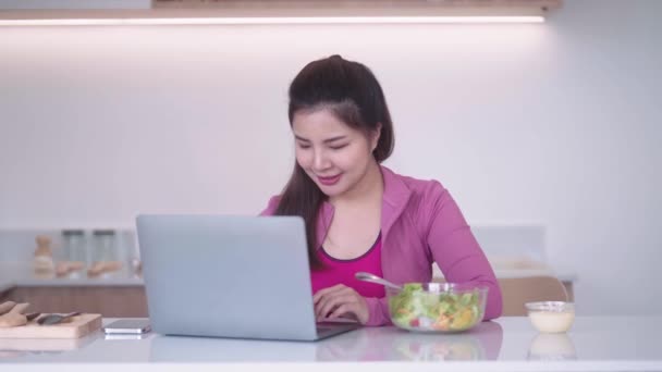 身穿运动服的年轻亚洲女运动员看着笔记本电脑 在厨房里吃着蔬菜沙拉 健康的饮食和运动理念 高质量的4K镜头 — 图库视频影像