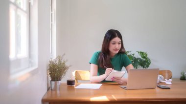 Genç Asyalı kadın öğrenciler online derste ders çalışmak ve izlemek için bilgisayarlarını kullanırken aynı zamanda evden uzaktan eğitimi ve not defterine bilgi yazmayı öğreniyorlar..