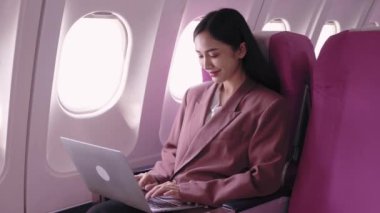 Asyalı bir iş kadını dizüstü bilgisayarı üzerinde çalışıyor, uçuş sırasında görevleri aktif olarak kaydediyor ve analiz ediyor. Ulaşım sırasında verimliliği maksimuma çıkarmaya kendini adadı.. 