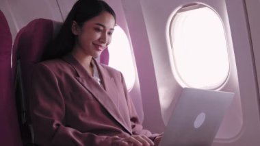 Asyalı bir iş kadını dizüstü bilgisayarı üzerinde çalışıyor, uçuş sırasında görevleri aktif olarak kaydediyor ve analiz ediyor. Ulaşım sırasında verimliliği maksimuma çıkarmaya kendini adadı.. 