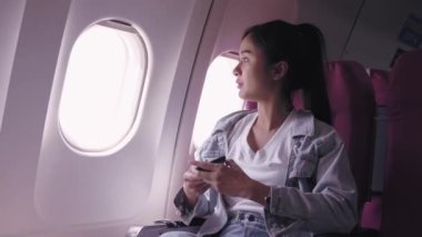 Şu anda bir uçak yolculuğunda olan Asyalı kadın turistler, o anın güzelliğine dalmış bir şekilde, uçağın penceresinden gökyüzünün fotoğraflarını çekiyorlar..