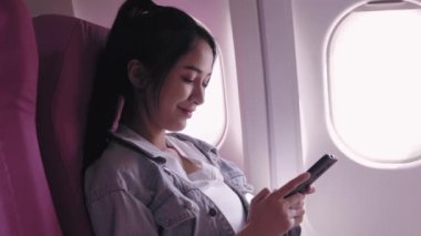 Asyalı kadın turistler şu anda uçakla seyahat ediyorlar ve cep telefonlarıyla gezilerini keşfediyorlar, neşeli ve etkileyici anları yakalıyorlar., 