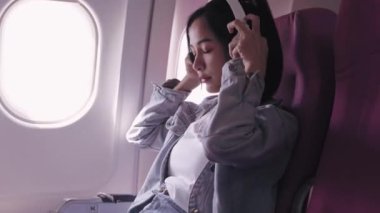 Şu anda bir uçak yolculuğunda olan Asyalı kadın gezginler, kulaklıklarıyla mutlu bir şekilde müzik dinliyorlar ve yavaşça mırıldanıyorlar. Bu mutluluk ve rahatlama çağrıştırır..