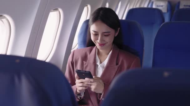 アジアのビジネスマンは 飛行機で旅行中に情熱的に仕事を記録し分析するために彼女の携帯電話を使用しています 飛行中にタスクを効率的に管理する — ストック動画