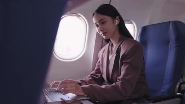 An Asian businesswoman is working on her laptop, actively recording and analyzing tasks during her flight. She is dedicated to maximizing productivity while in transit