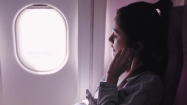 Şu anda bir uçak yolculuğunda olan Asyalı kadın gezginler, kulaklıklarıyla mutlu bir şekilde müzik dinliyorlar ve yavaşça mırıldanıyorlar. Bu mutluluk ve rahatlama çağrıştırır..